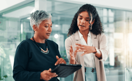 Two women engaged in conversation while looking at a tablet together.