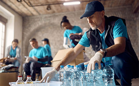 Volunteers organizing supplies, with a man in a cap packing water bottles.